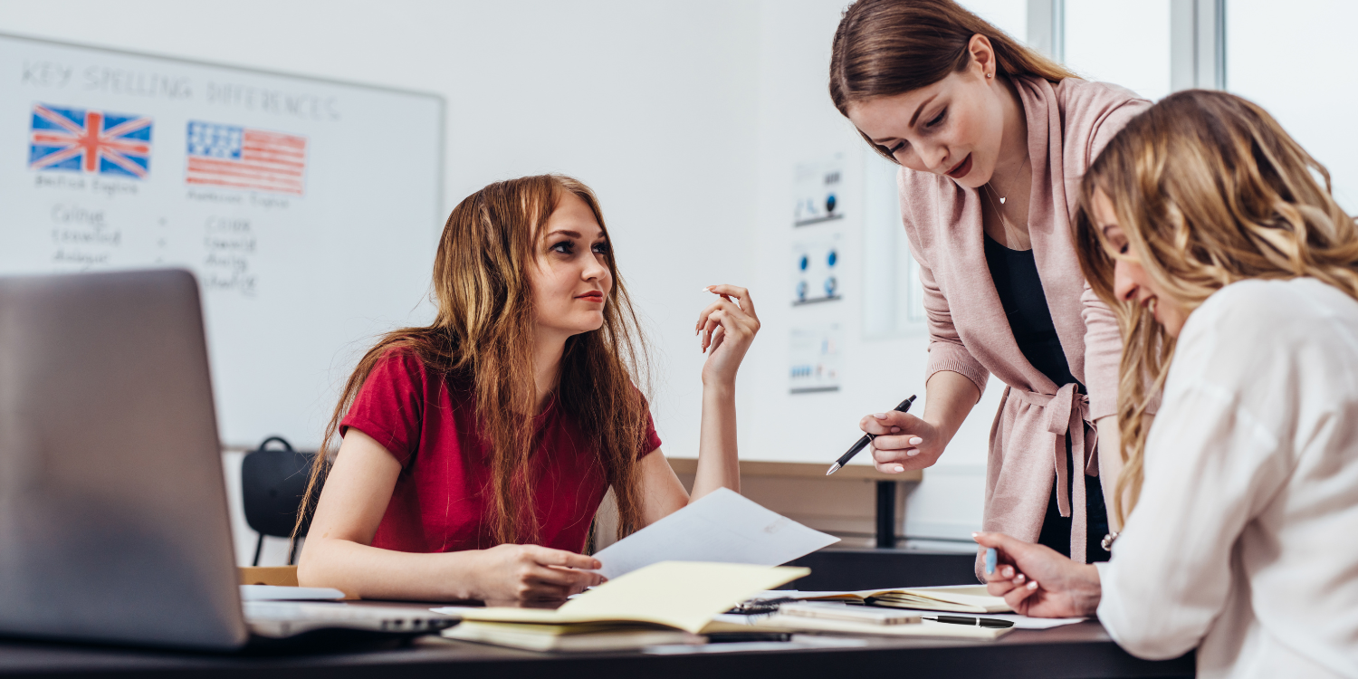 Zwei Frauen in einem Englischkurs lassen sich die Aufgabe genau von der Englischlehrerin erklären.