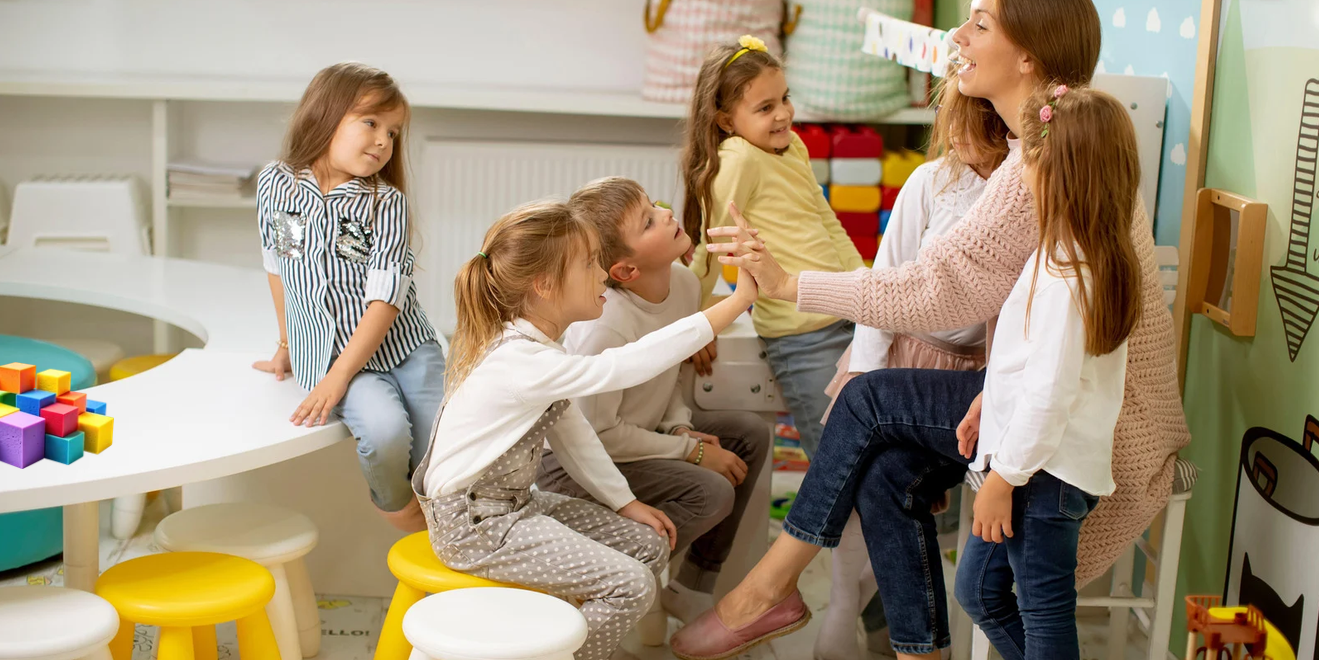 Ein Kinderbetreuuerin spielt mit einer Gruppe von Kindern im Alter von 5 bis 7 Jahren